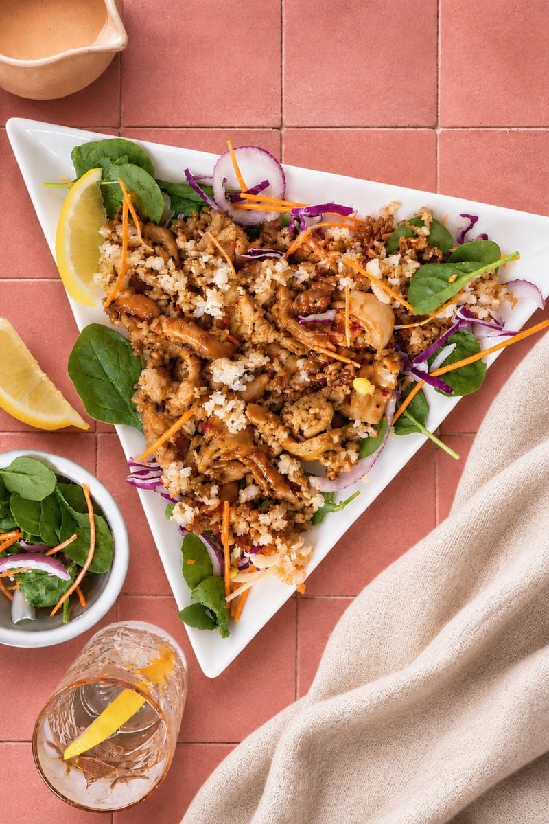 Crispy rice chicken salad with golden chicken, crunchy rice, fresh spinach, shredded carrots and red cabbage on a white serving plate.
