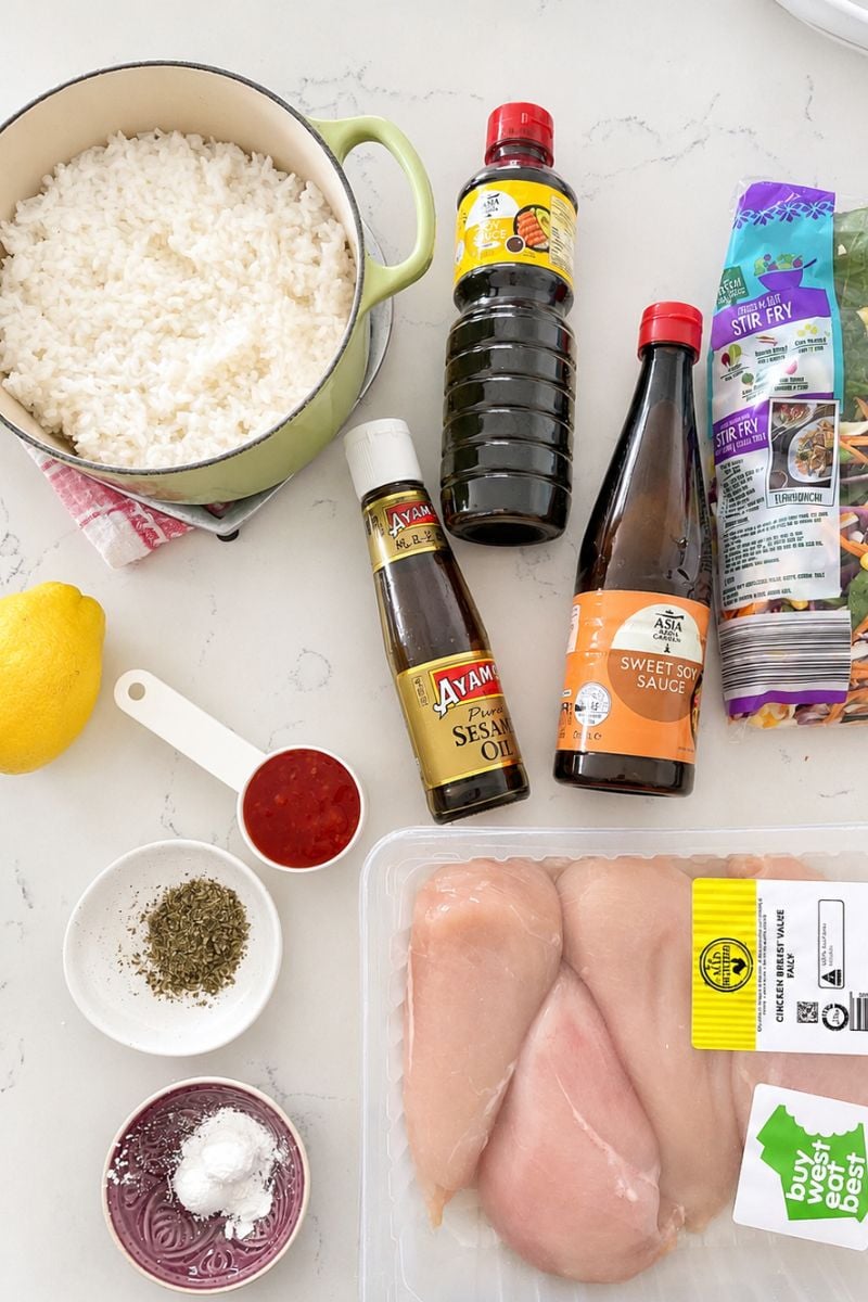 Ingredients for crispy rice chicken salad, including cooked rice, raw chicken, soy sauce, sesame oil, lemon, sweet chilli sauce and mixed vegetables.