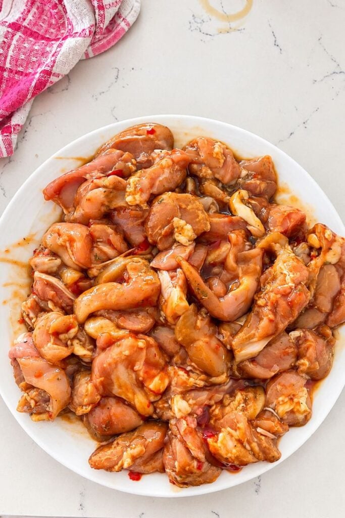 Raw chicken pieces coated in a sweet and savoury marinade in a white bowl, ready for cooking.