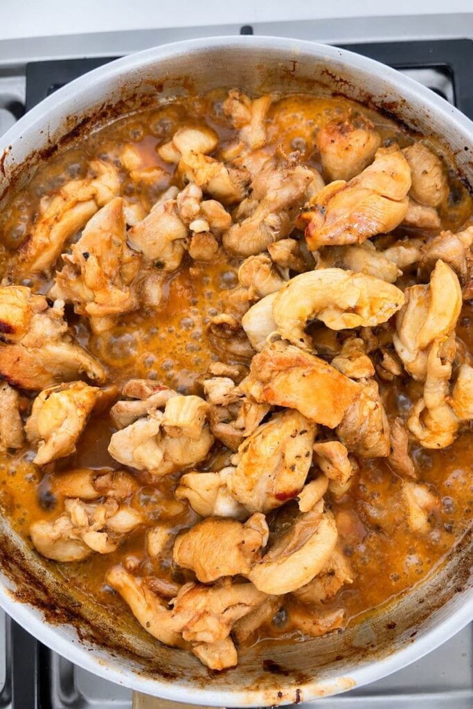 Marinated chicken pieces simmering in a frying pan with a rich, glossy sauce until golden and cooked through.