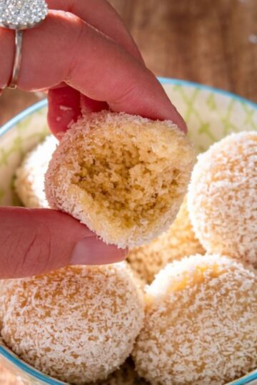 Holding a lemon energy ball covered in coconut.