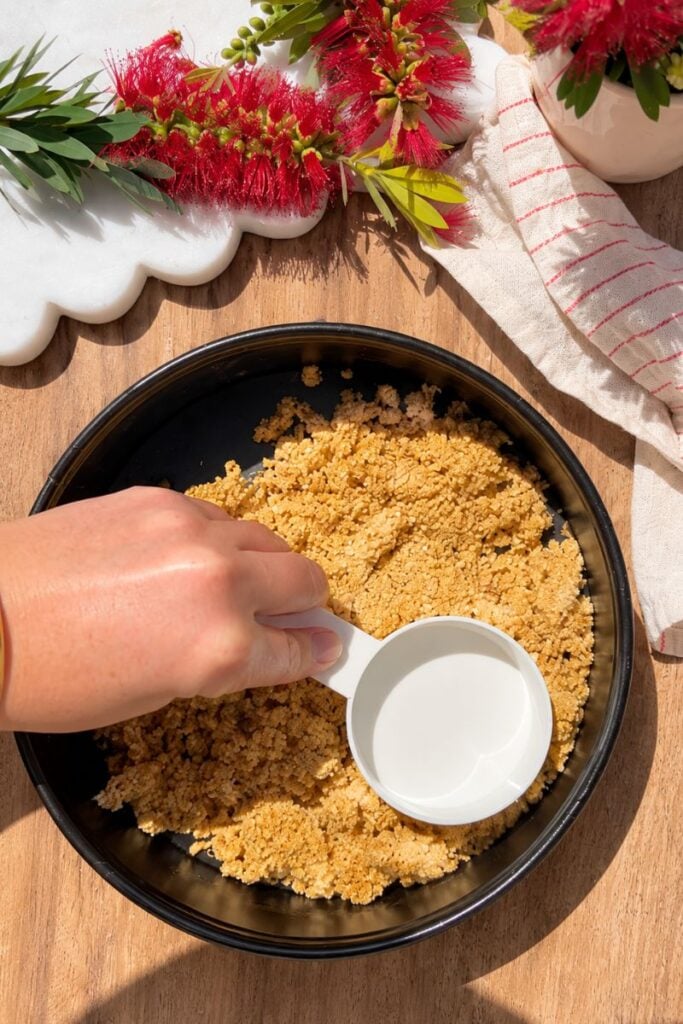 Pressing the oat crust into a baking pan for pumpkin cottage cheese cheesecake.