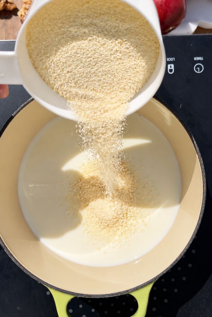 Fine semolina being added slowly to warm milk in a saucepan.