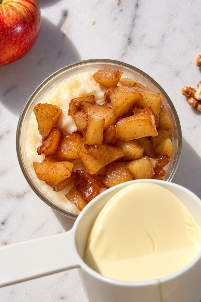 Cream being poured over semolina pudding with warm spiced apples.